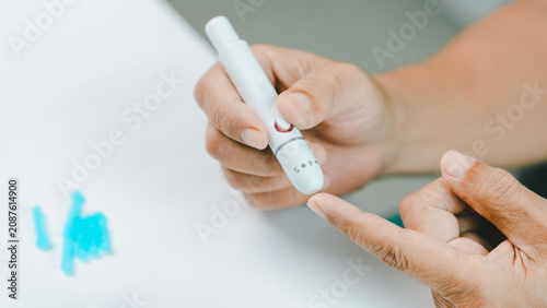 Tableau sur toile Close-up of a senior adult preparing a finger prick with a lancet device for blood glucose testing at home