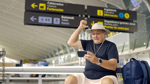 Man celebrating win on smartphone in airport terminal