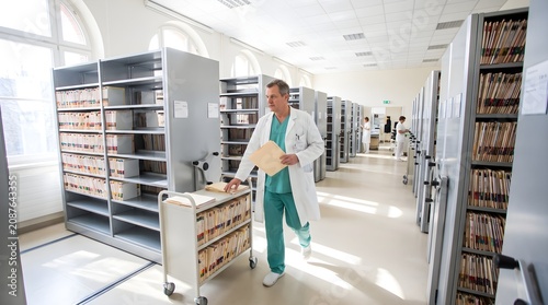 Middle aged male doctor pushing medical record cart through sterile hospital archives