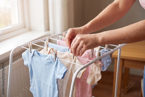 Mother Hanging Baby Clothes on Drying Rack at Home