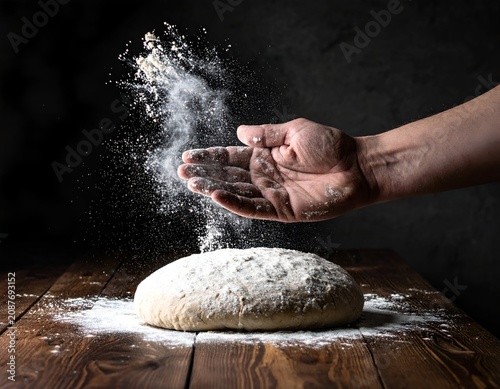 Baker hands dusting fine white flour over fresh bread dough on a dark rustic wooden worktable