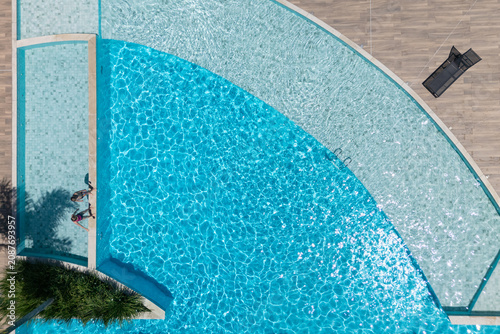 Two kids relax at the edge of clear blue pool during sunny summer vacation. This aerial view captures family,  friends, fun, and recreation at resort, relaxation and joyful outdoor moments.