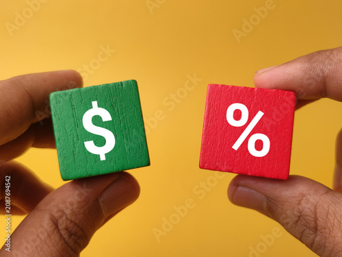 Two hands hold a green wooden cube with a dollar sign and a red cube with a percentage