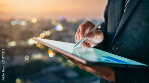 Businessman analyzing data on a tablet with a stylus, overlooking a city, symbolizing modern business and technology