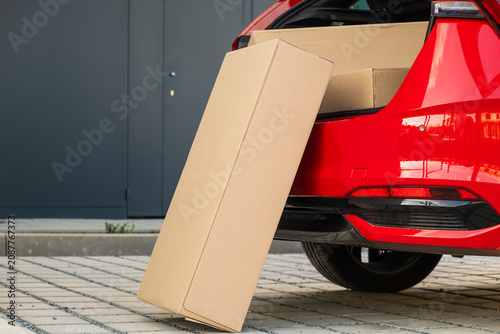 Cardboard shipping box partially removed from the rear hatch of a red compact vehicle.