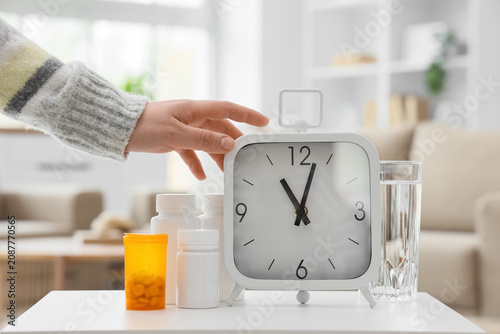 Foto Female hand with clock, pills and glass of water on table in room