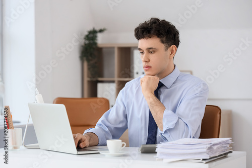 Thoughtful young businessman working with laptop at desk in office