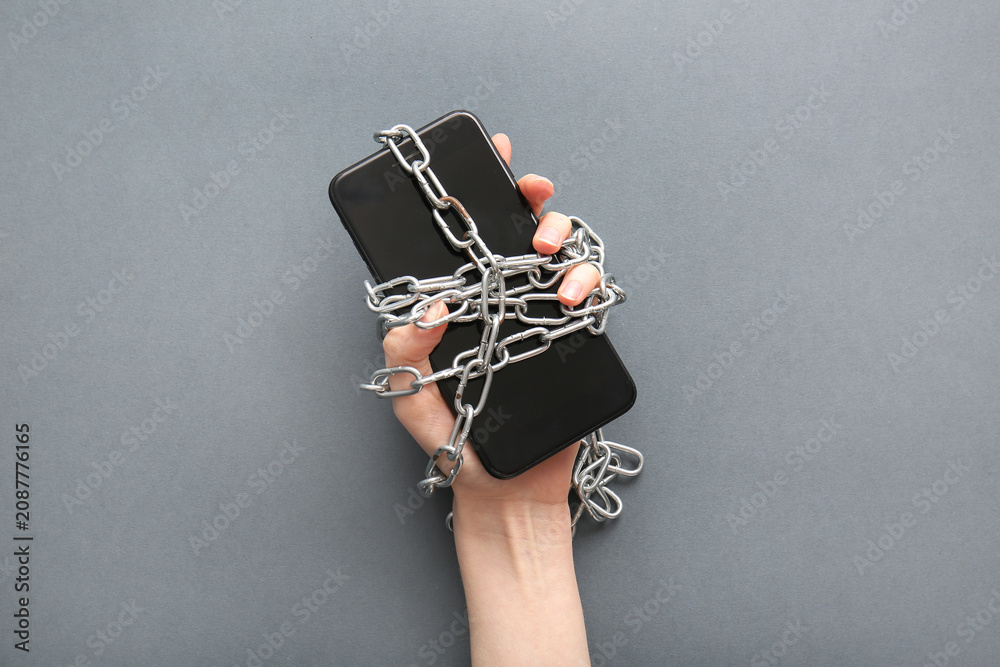Obraz premium Female hand with modern mobile phone and chain on grey background, closeup