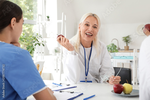 Female doctor eating apple at table in clinic