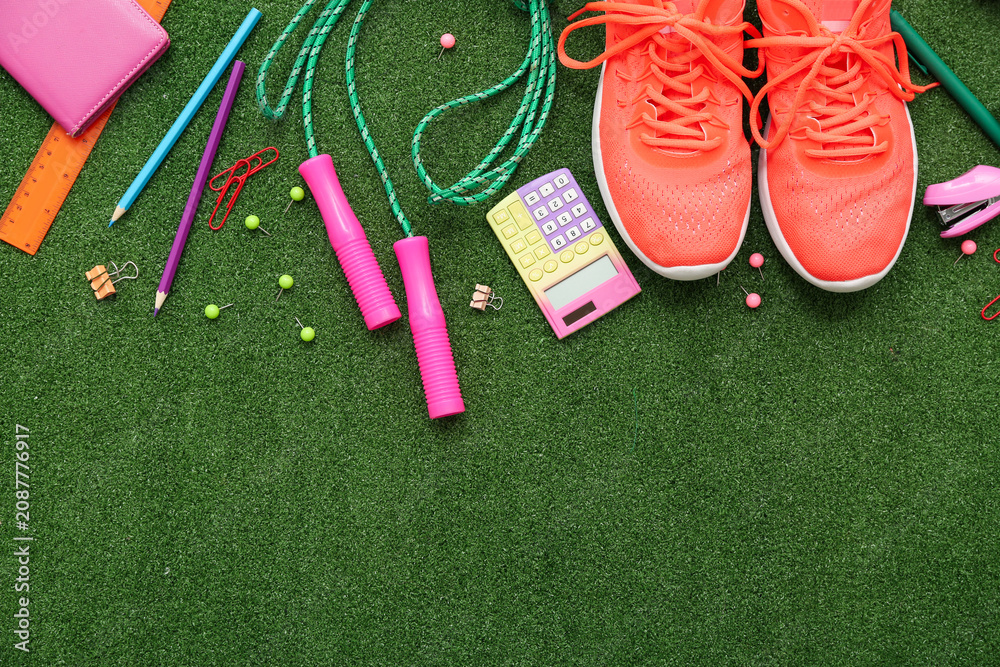 Obraz premium Sneakers, jumping rope and different stationery on artificial grass as background