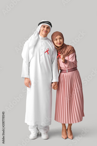 Beautiful Muslim couple with red ribbons on grey background. AID awareness co...