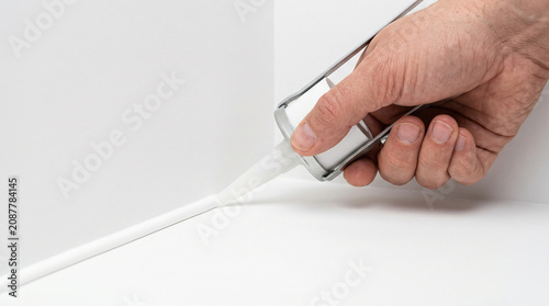 Hand using a caulking gun to apply white sealant along a corner