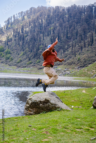 Hiker jumping for joy by Kareri Lake in the mountains of Dharamshala Himachal Pradesh India