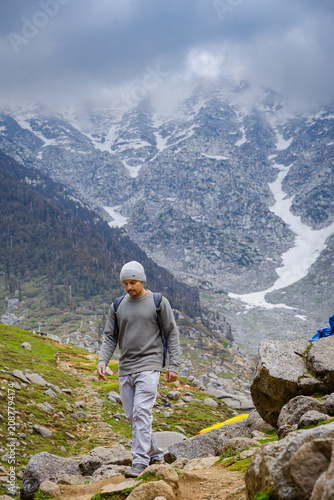 Hiker trekking on a rocky mountain trail at Kareri Lake in Dharamshala with snowy peaks in background