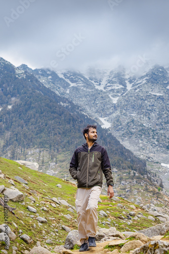 Young man hiking on a rocky mountain trail at Kareri Lake in Dharamshala with a scenic cloudy view
