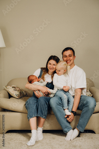 A family portrait of parents with a newborn baby and an older daughter on the sofa.
