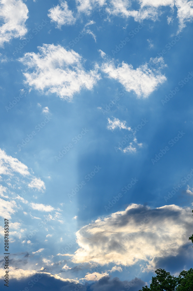 Obraz premium Bright sun rays breaking through white clouds into a vivid blue summer sky