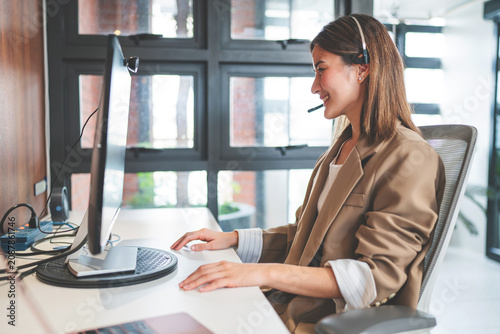Canvastavla Friendly smiling woman call center operator with headset using computer, Customer service, Call center worker accompanied by her team at office
