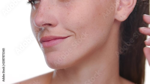 Extreme closeup of Spanish woman with fair skin and freckles strokes a jawline presenting revitalized skin against white bg | Face care concept