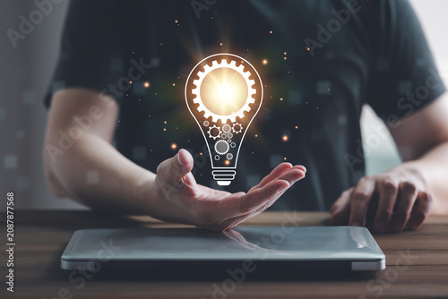 Creative innovation concept with a glowing light bulb and gear icon above laptop computer, representing problem solving, business strategy, technology, engineering, productivity and smart idea.