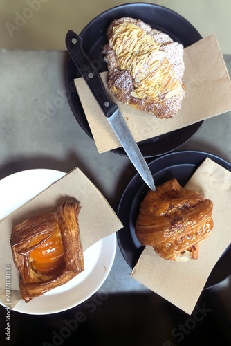Top view of assorted artisan pastries served on ceramic plates in a modern café. Freshly baked croissants, Danish pastry, and laminated pastries with powdered sugar and fruit filling