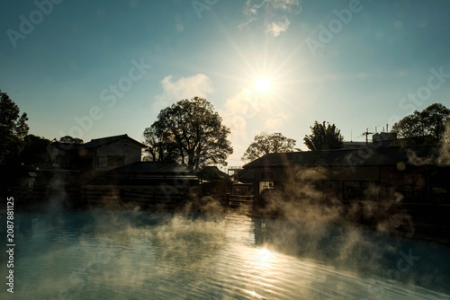 Beautiful morning scenery of a steaming thermal hot spring pool reflecting bright sunlight.
