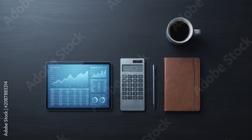 A professional financial analyst workspace featuring a digital tablet showing stock market charts, a calculator, a notebook, and a cup of coffee on a dark desk for business planning and data analysis