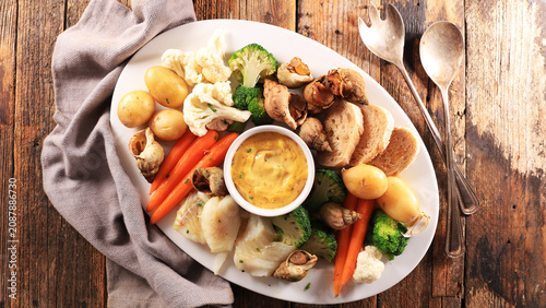 Top view of traditional french aioli platter with cod fish and sea snails on rustic wood