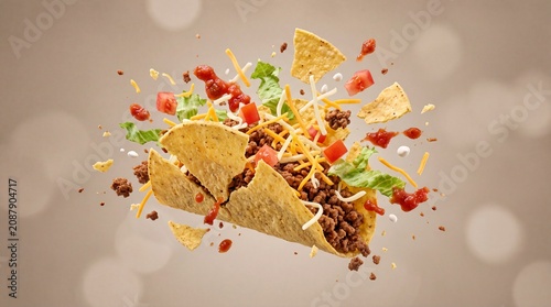 Exploding beef taco with flying ingredients, dynamic food splash of crispy tortilla shells and fresh toppings, mexican cuisine action shot