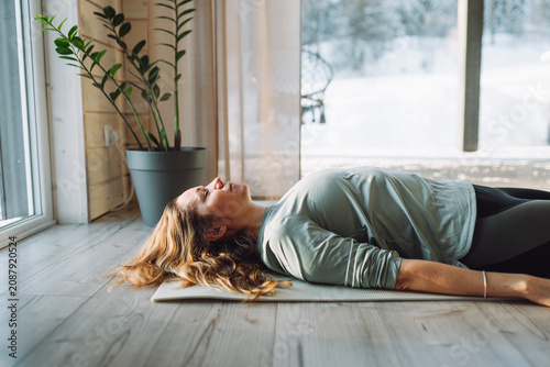 Mature woman doing corpse pose on exercise mat at home