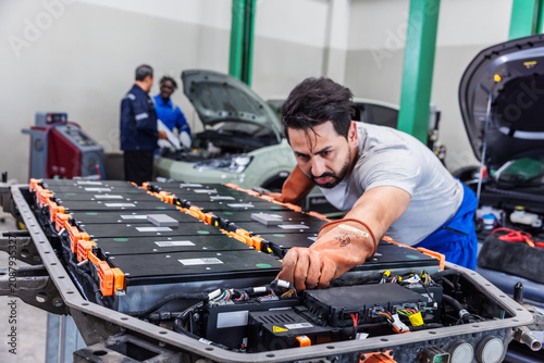 Confident electric vehicle technician smiling beside a high-voltage battery pack during maintenance in a modern EV service center.