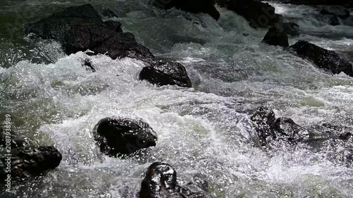 Slow motion of rapid water stream crashing against black stones in a forest creek. Fresh natural water rushing down the river, mindfulness and nature concept.