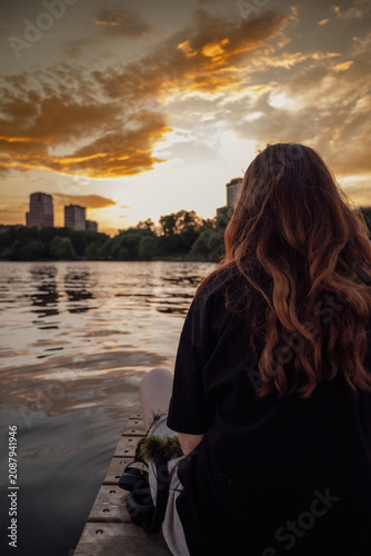 Red haired woman looking at sunset over river and city