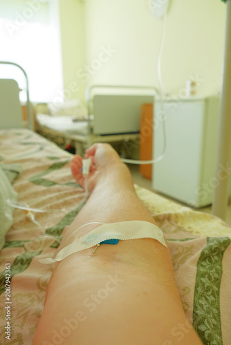 Patient lying in a hospital bed with a peripheral intravenous catheter inserted into the arm, receiving infusion therapy. Close-up of IV access for medical treatment and healthcare