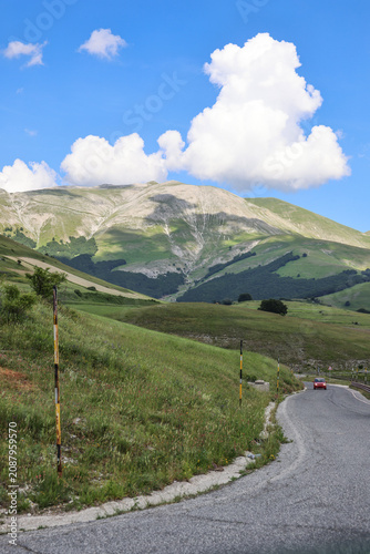 Foto Winding Mountain Road with a Driving Red Car, Castelluccio di Norcia, Italy