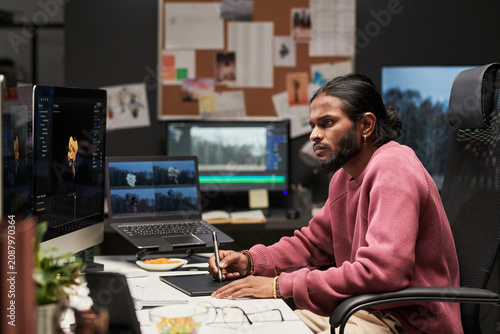 Foto Young man editing video at workstation, using pen tablet and multiple screens for postproduction workflow