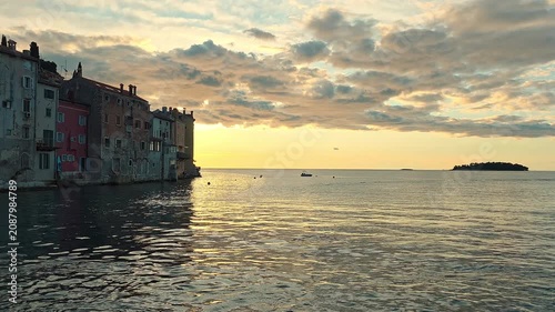 Warm sunset over Rovinj old town waterfront and calm Adriatic sea, golden video frame with historic homes, soft clouds, small island and water reflections