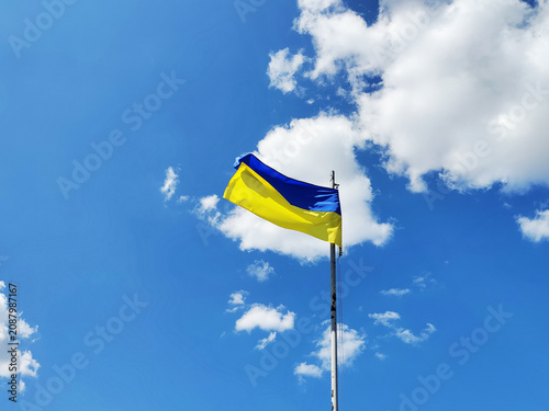 Photo of Ukrainian flag waving against blue sky with white clouds. Mobile photography. National flag outdoors.
