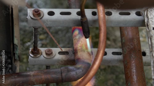 Close-up of brazing copper pipes with a gas torch with a distinctive green flame. Professional plumbing repair or HVAC air conditioning installation process, industrial soldering connection