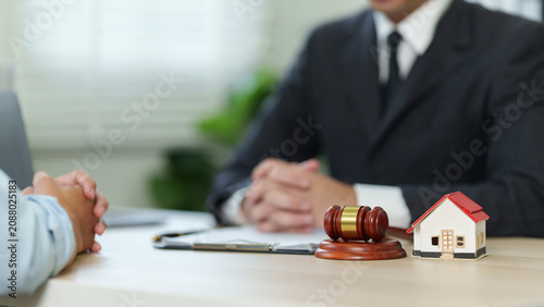 Real estate lawyer consulting client with model house and gavel on desk