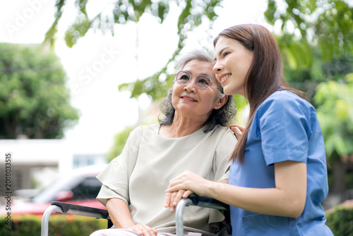 Young caucasian nurse comforting with patient while sitting on wheelchair in outdoor park, doctor woman support and counseling with patient, caregiver and service with senior, medical and consoling.