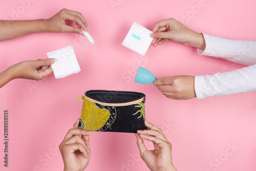 Multiple Hands Reach Towards Open Pouch Holding Tampon Menstrual Cup And Pads To Pack