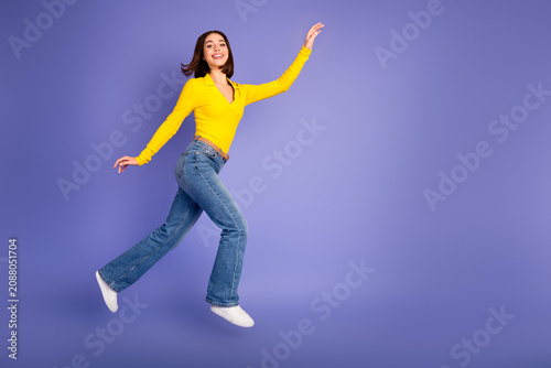 Cuadro en lienzo Young chic woman in yellow top and jeans jumping against purple background for a