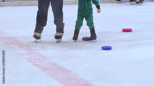 Close up of child feet learning to skate on ice skating rink. Figure skating, ice skating training. Little boy learning how to ice skate on indoor ice skating rink.