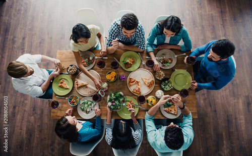 Cuadro en lienzo Friends gathered around a wooden table sharing pizza, salad and wine during a ca
