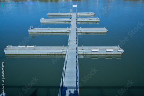A high angle detailed landscape photograph showing an empty grey floating boat dock jetty pier structure upon calm blue river water during a bright sunny spring day