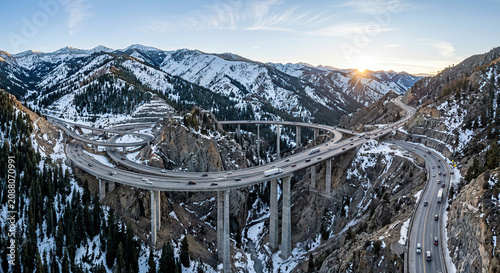 Aerial view of an elevated highway bridge crossing through snowy mountains at sunset.
