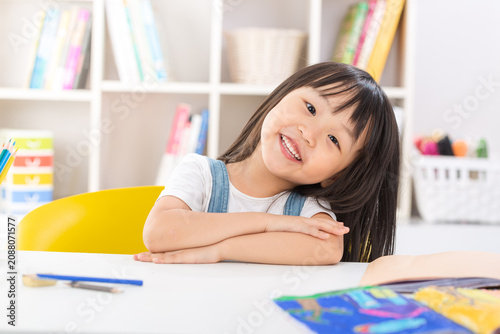 Foto A polite and happy little Asian girl sitting up straight at her desk with crossed arms and smiling brightly at the camera