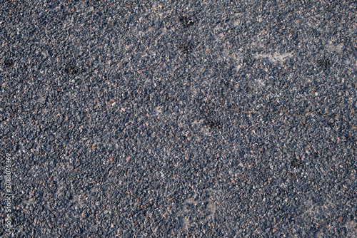 Dark asphalt surface shows coarse, uneven texture. Gravel and oil stains add worn, gritty appearance.