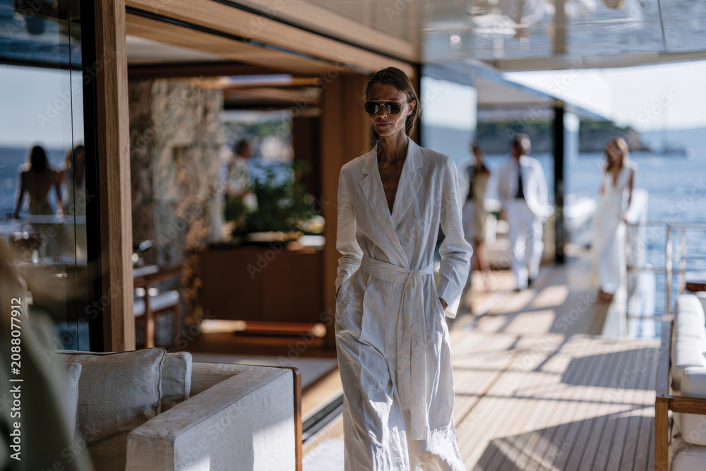 Fototapeta premium A chic woman strolls along the deck of a luxury yacht, radiating confidence and style as she immerses herself in the magnificent ocean views.